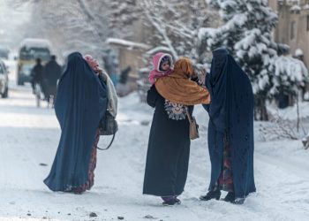 (FILES) In this file photo taken on January 23, 2023, Afghan burqa-clad women carry children as they walk along a snow laden street in Kabul. – At least 166 people have perished in a wave of bitterly cold weather sweeping Afghanistan, officials said January 28, as extreme conditions continue to heap misery on the poverty-stricken nation. (Photo by Wakil KOHSAR / AFP)