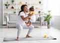 Workout With Baby. Cheerful Black Woman Exercising at Home with Infant Son, Sporty African American Female Training on Fitness Mat, Holding Her Cute Toddler Child and Making Squats, Copy Space