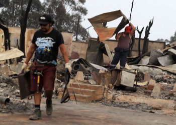 Men remove debris from houses destroyed by a forest fire in the hills of Tome, Concepcion province, Biobio region, Chile on February 4, 2023. – Chile has declared a state of disaster in several central-southern regions after a devastating heat wave provoked forest fires that left four people dead, authorities said on Friday. (Photo by JAVIER TORRES / AFP)