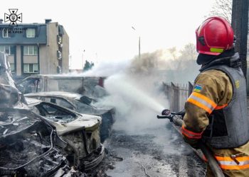 This handout photograph taken and released by the Ukrainian Emergency Service on March 9, 2023, shows a rescuer extinguishing vehicles at the site of fallen fragments of a rocket, near a multi-storey residential building. (Photo by Handout / UKRAINIAN EMERGENCY SERVICE / AFP) /