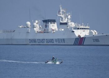 This photo taken on September 20, 2023 shows a Philippine fisherman aboard his wooden boat sailing past a Chinese coast guard ship near the Chinese-controlled Scarborough Shoal in disputed waters of the South China Sea. – China, which claims sovereignty over almost the entire South China Sea, snatched control of Scarborough Shoal from the Philippines in 2012. Since then, it has deployed coast guard and other vessels to block or restrict access to the fishing ground that has been tapped by generations of Filipinos. (Photo by Ted ALJIBE / AFP)